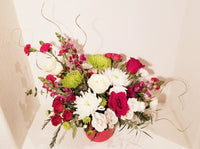 Christmas Magic Arrangement in red vase. An array of winter fresh cut flowers of the holiday arranged including Roses, spray, Snapdragons, Chrysanthemums, buttons and winter greenery