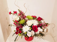 Christmas Magic Arrangement in red vase. An array of winter fresh cut flowers of the holiday arranged including Roses, spray, Snapdragons, Chrysanthemums, buttons and winter greenery